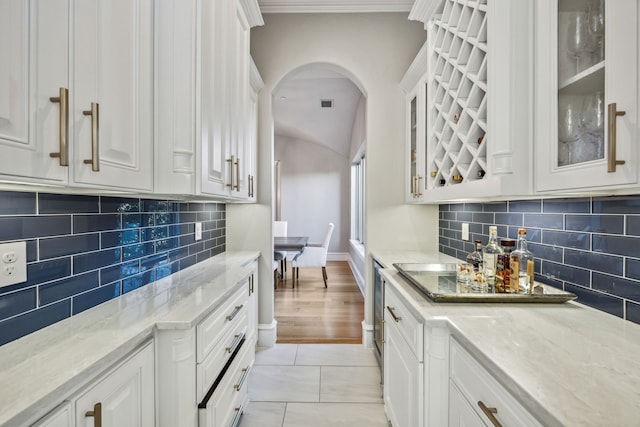 6800 Rainwood Dr, Plano, TX 75024 - kitchen with white cabinetry, arched walkways, decorative backsplash, light stone counters, and glass insert cabinets