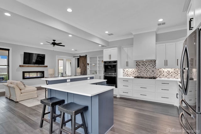 kitchen featuring white cabinetry, a barn door, appliances with stainless steel finishes, a kitchen island, and custom exhaust hood