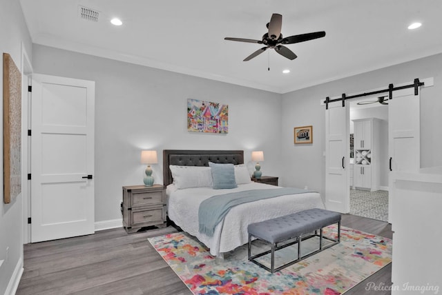 bedroom featuring wood-type flooring, a barn door, ornamental molding, and ceiling fan