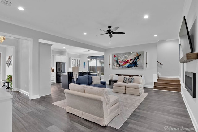 living room with ornamental molding, ceiling fan with notable chandelier, and dark wood-type flooring