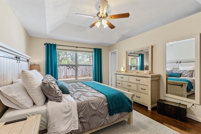 bedroom with a textured ceiling, lofted ceiling, ceiling fan, and dark wood-type flooring