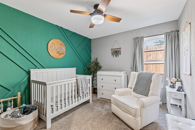 bedroom featuring a nursery area, carpet, and ceiling fan