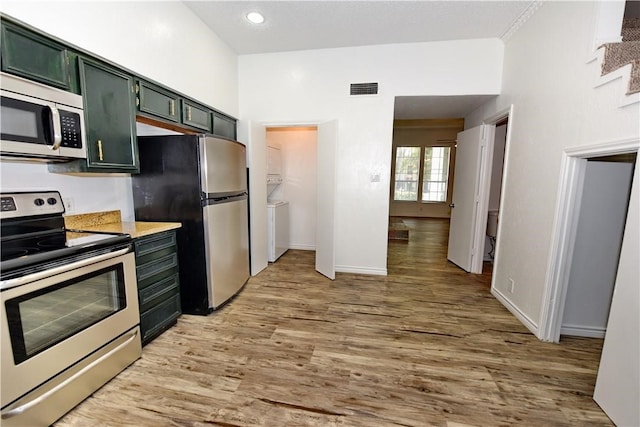 kitchen with stainless steel appliances, washer / dryer, green cabinets, and light hardwood / wood-style flooring