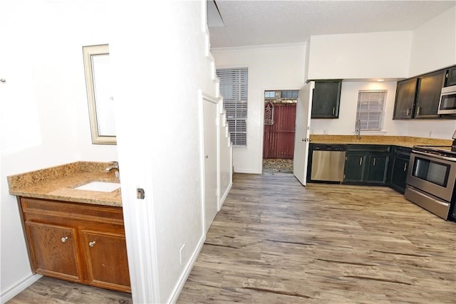 kitchen with ornamental molding, appliances with stainless steel finishes, light stone countertops, sink, and light hardwood / wood-style floors