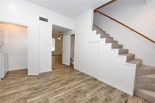 stairs featuring hardwood / wood-style floors, stacked washer and dryer, and ceiling fan