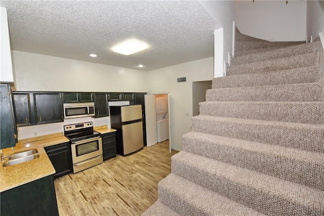 kitchen featuring a textured ceiling, sink, light wood-type flooring, appliances with stainless steel finishes, and washer / dryer