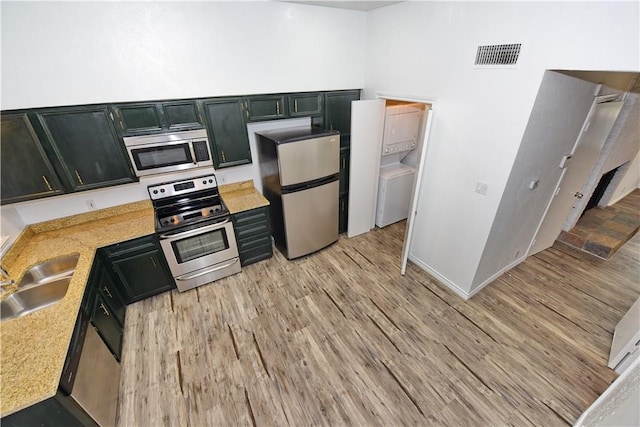 kitchen featuring stacked washer and clothes dryer, stainless steel appliances, light stone countertops, sink, and light hardwood / wood-style floors