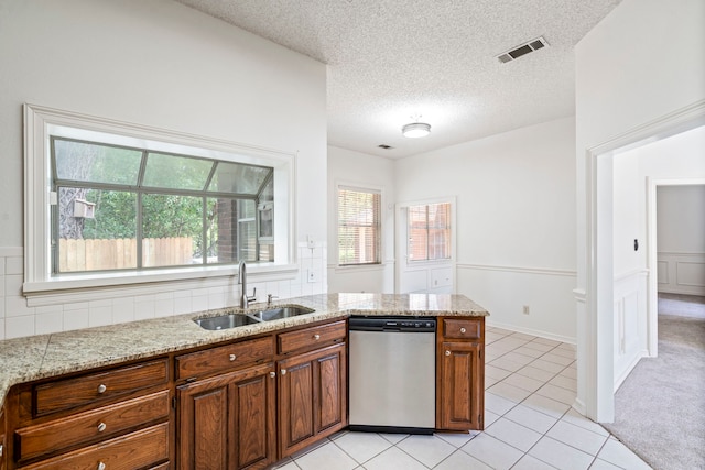 kitchen featuring a textured ceiling, light stone counters, stainless steel dishwasher, and sink