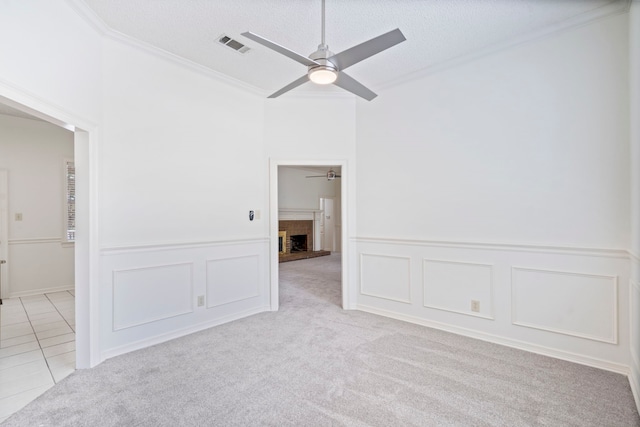 carpeted empty room with a textured ceiling, ceiling fan, ornamental molding, and a fireplace