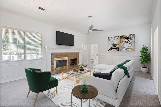 carpeted living room featuring ceiling fan, ornamental molding, a textured ceiling, and a brick fireplace