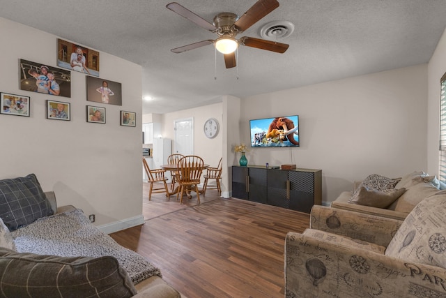 living room featuring dark wood-type flooring, ceiling fan, and a textured ceiling