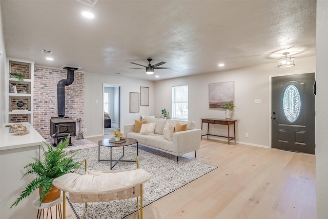 living room with ceiling fan, a wood stove, a textured ceiling, and light hardwood / wood-style flooring