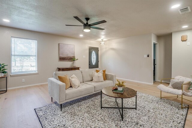 living room with ceiling fan, a textured ceiling, and light wood-type flooring