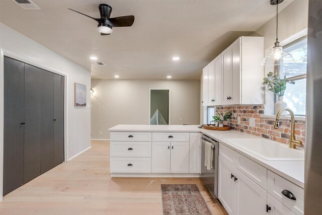 kitchen featuring stainless steel dishwasher, sink, white cabinets, light hardwood / wood-style flooring, and pendant lighting