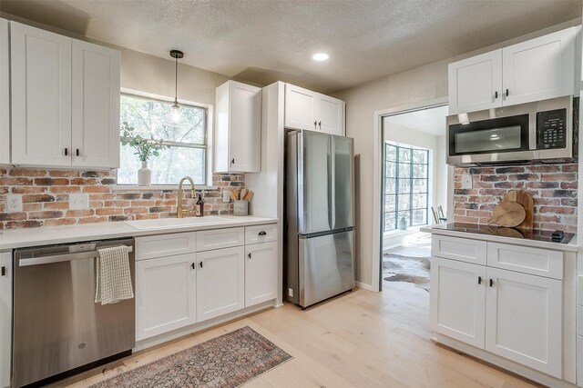 kitchen featuring white cabinets, sink, light wood-type flooring, decorative light fixtures, and stainless steel appliances