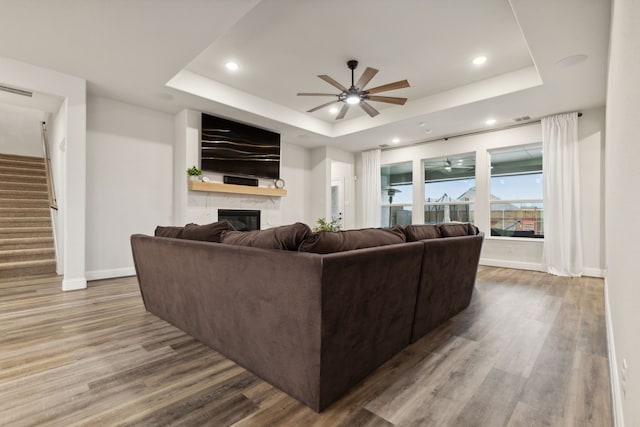 living room with a tray ceiling, ceiling fan, and wood-type flooring