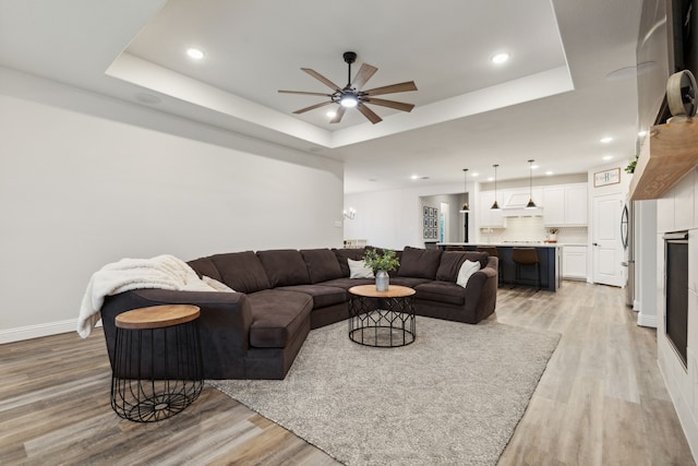 living room with a tray ceiling, ceiling fan, and light hardwood / wood-style flooring