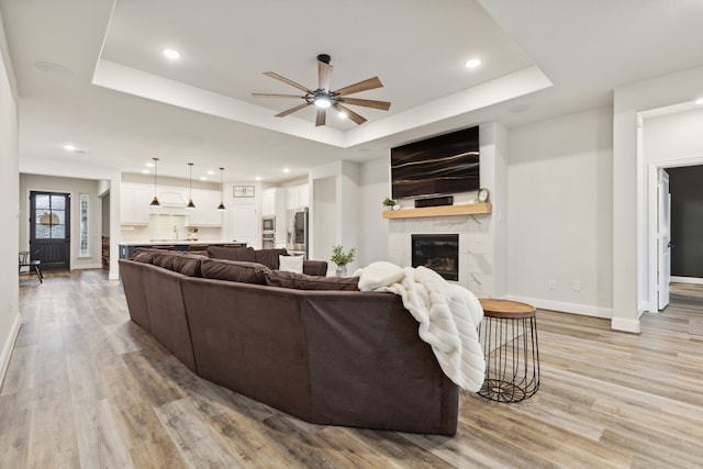 living room with a fireplace, light hardwood / wood-style floors, a raised ceiling, and ceiling fan