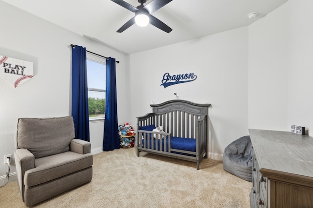 carpeted bedroom featuring ceiling fan and a crib