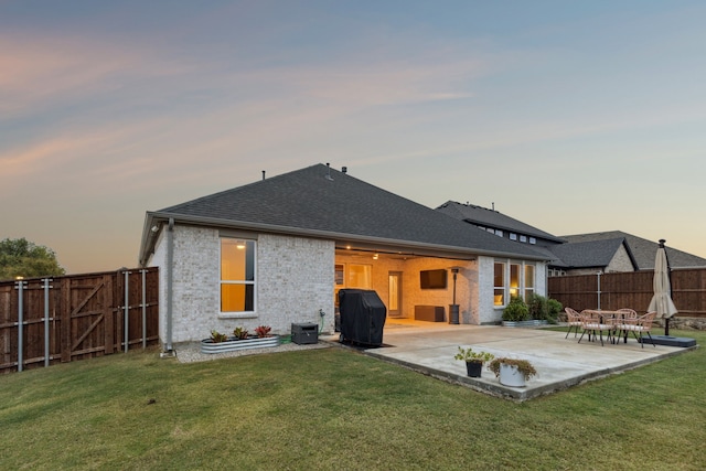 back house at dusk featuring a yard and a patio