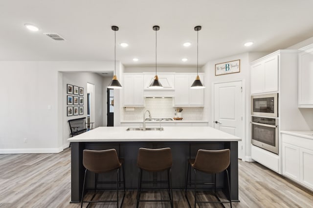 kitchen featuring an island with sink, stainless steel appliances, decorative light fixtures, and light wood-type flooring