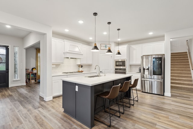 kitchen with an island with sink, sink, white cabinets, and stainless steel appliances