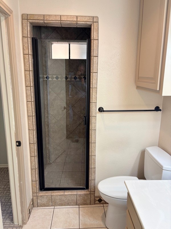 bathroom featuring tile patterned flooring, vanity, toilet, and a shower with door