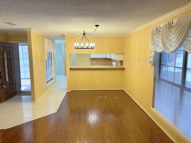 kitchen with ornamental molding, a textured ceiling, a notable chandelier, light hardwood / wood-style floors, and kitchen peninsula