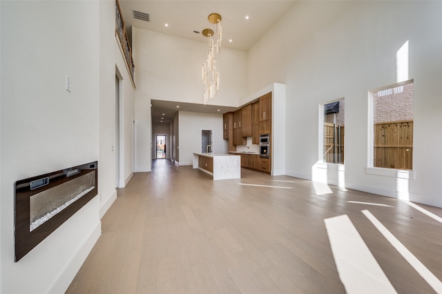 unfurnished living room with a high ceiling, light hardwood / wood-style floors, and a notable chandelier