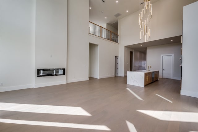 unfurnished living room with heating unit, hardwood / wood-style floors, a notable chandelier, and a towering ceiling