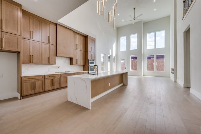 kitchen with ceiling fan with notable chandelier, a center island with sink, light stone counters, light hardwood / wood-style flooring, and a high ceiling