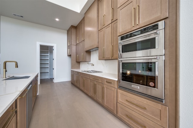 kitchen featuring stainless steel appliances, light stone countertops, sink, and light wood-type flooring