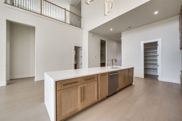 kitchen featuring sink, an island with sink, stainless steel dishwasher, light hardwood / wood-style flooring, and a high ceiling