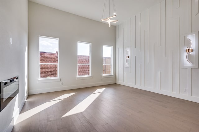 spare room featuring light wood-type flooring, a healthy amount of sunlight, and an inviting chandelier