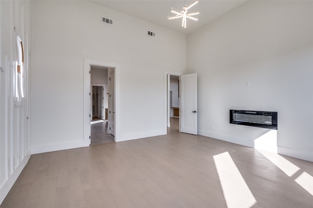 empty room featuring high vaulted ceiling, light wood-type flooring, and an inviting chandelier