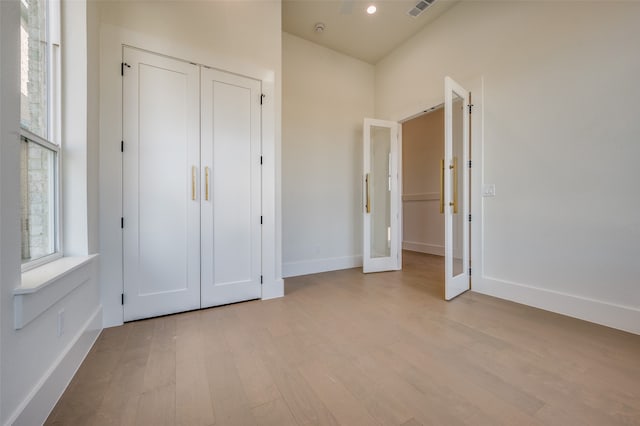 unfurnished bedroom featuring french doors, light wood-type flooring, and a closet