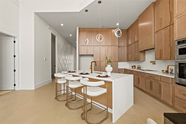 kitchen with cooktop, a kitchen bar, pendant lighting, double oven, and a kitchen island with sink