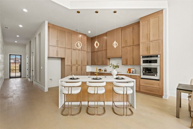 kitchen featuring stainless steel double oven, decorative light fixtures, a center island with sink, and a breakfast bar