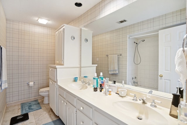 bathroom with tile walls, tile patterned floors, walk in shower, vanity, and toilet