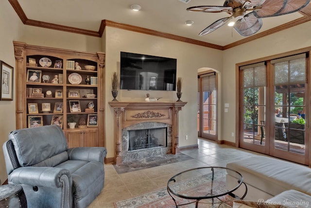 tiled living room with a high end fireplace, ceiling fan, and crown molding