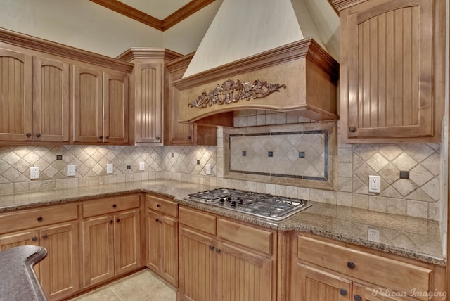 kitchen with stainless steel gas stovetop, decorative backsplash, crown molding, light stone countertops, and premium range hood