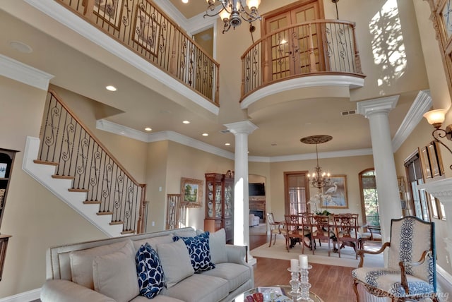 living room with wood-type flooring, a notable chandelier, crown molding, and a towering ceiling