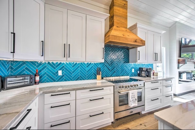 kitchen with custom range hood, white cabinetry, and range with two ovens