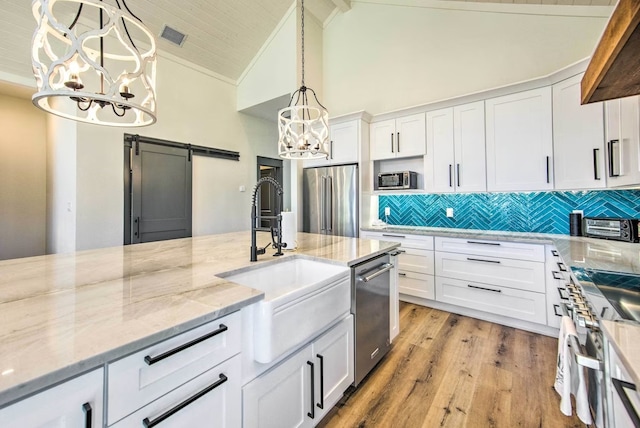 kitchen with white cabinetry, light wood-type flooring, a barn door, premium appliances, and pendant lighting