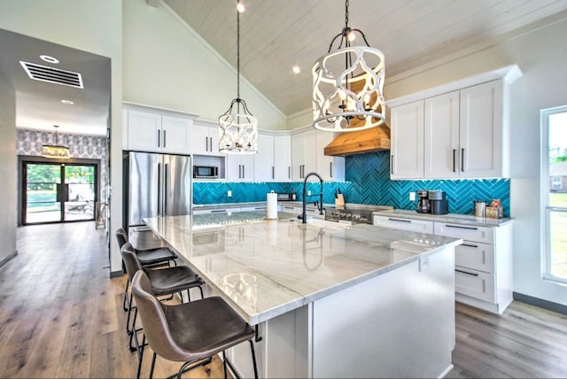 kitchen featuring white cabinets, high vaulted ceiling, appliances with stainless steel finishes, and a center island with sink