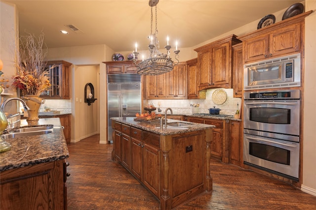 kitchen with built in appliances, a kitchen island with sink, sink, and dark hardwood / wood-style floors