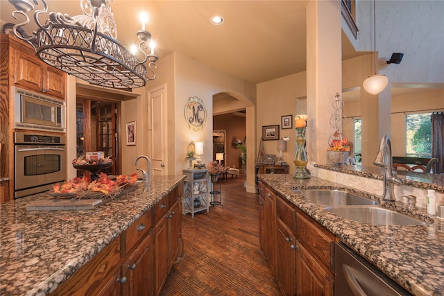 kitchen with appliances with stainless steel finishes, dark hardwood / wood-style flooring, sink, decorative light fixtures, and dark stone countertops