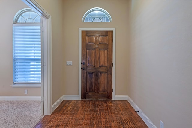 entryway featuring a towering ceiling, a healthy amount of sunlight, and dark colored carpet