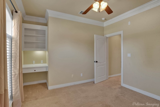 unfurnished bedroom with built in desk, light colored carpet, ceiling fan, and crown molding