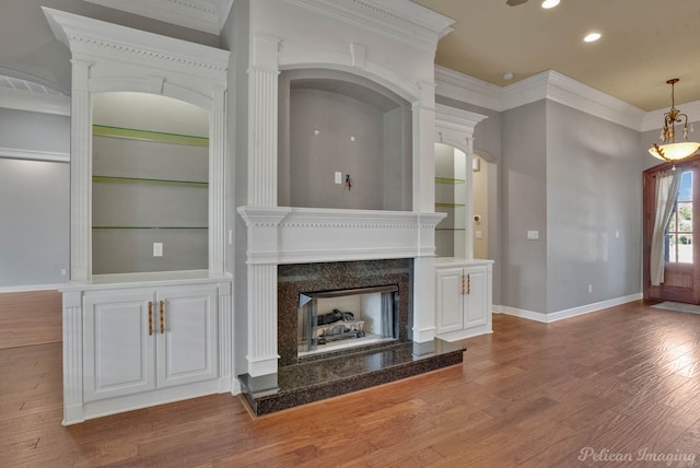 unfurnished living room featuring hardwood / wood-style flooring, built in features, crown molding, and a premium fireplace